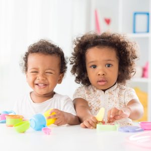 Portrait of a little girl posing at camera while her brother laughing and playing in the nursery
