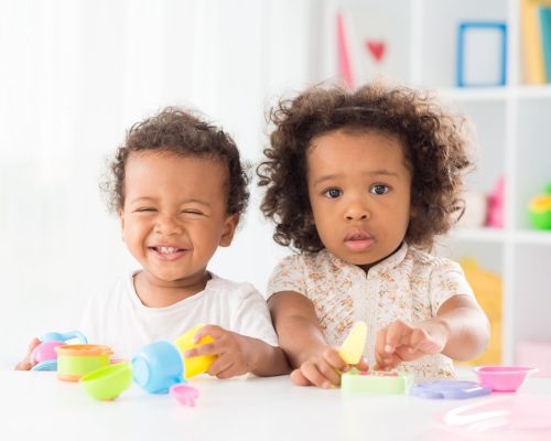 Portrait of a little girl posing at camera while her brother laughing and playing in the nursery