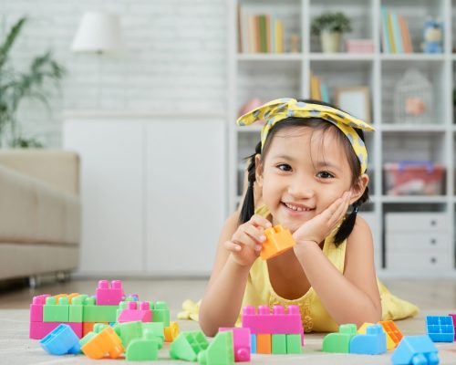 Portrait of smiling little girl lying on floor and playing with cubes